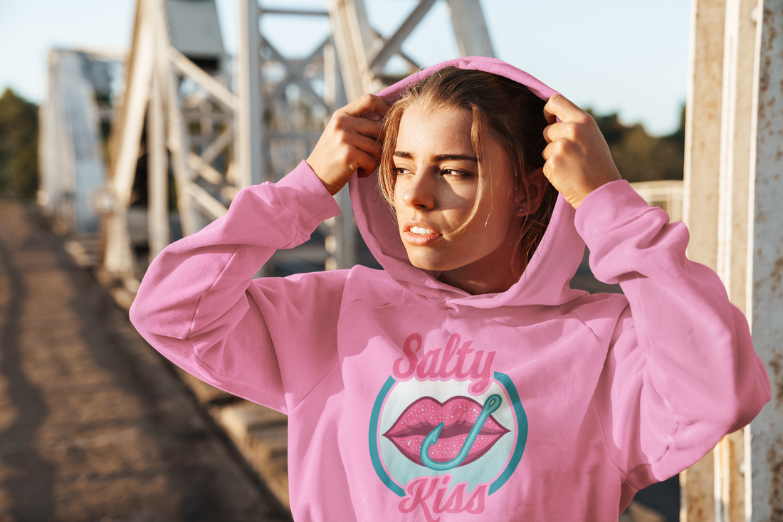 Salty Kiss youth coastal hoodie in pink worn on a sunny dockside boardwalk.