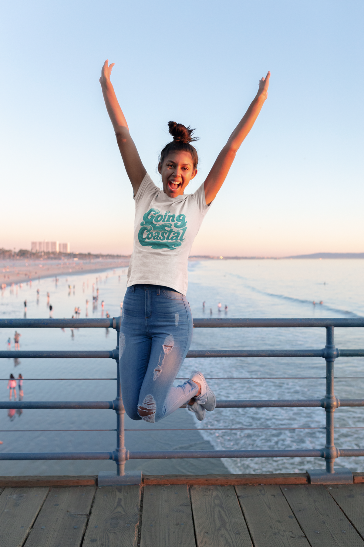 Salty Kiss women’s coastal graphic tee worn by a woman jumping on a beach pier by the ocean.