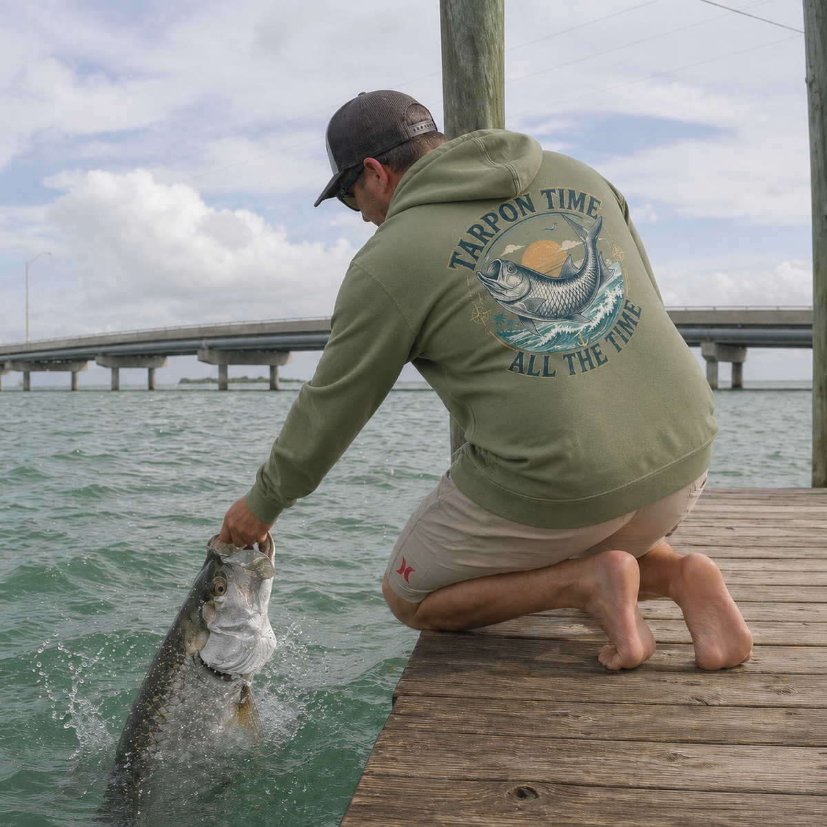 Salty Kiss men’s coastal fishing hoodie worn on a dock while handling a fish by the water in key west.