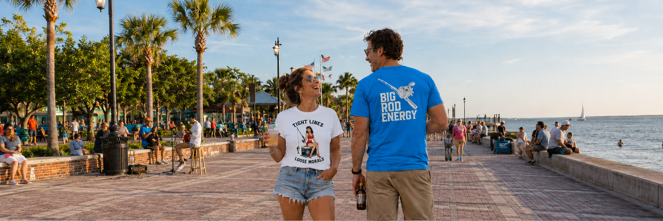 Salty Kiss men’s and women’s coastal graphic t-shirts worn on a sunny waterfront boardwalk.