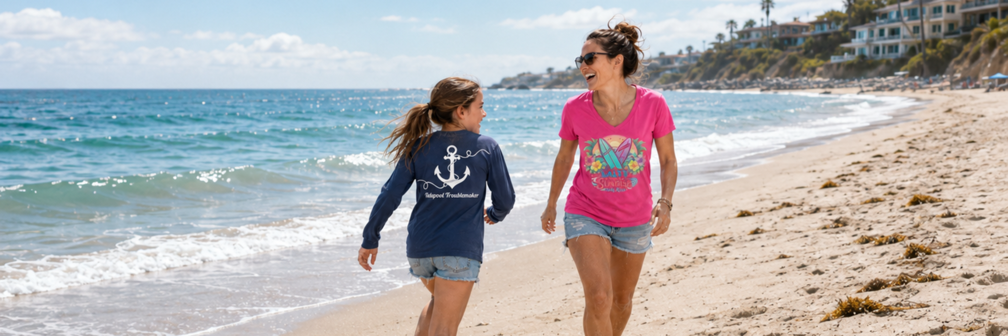 Salty Kiss women’s coastal tee and Tidepool Troublemaker youth shirt worn on a sunny beach walk.