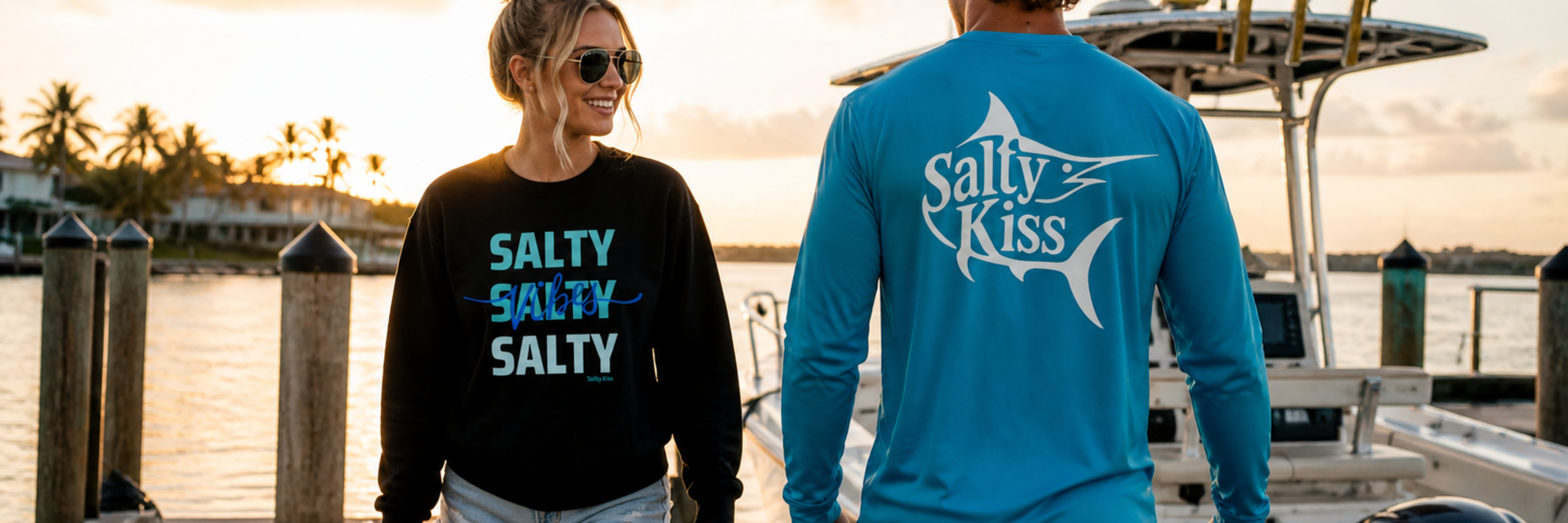 Man and woman wearing Salty Kiss fishing and coastal lifestyle t-shirts on a sunny waterfront boardwalk.