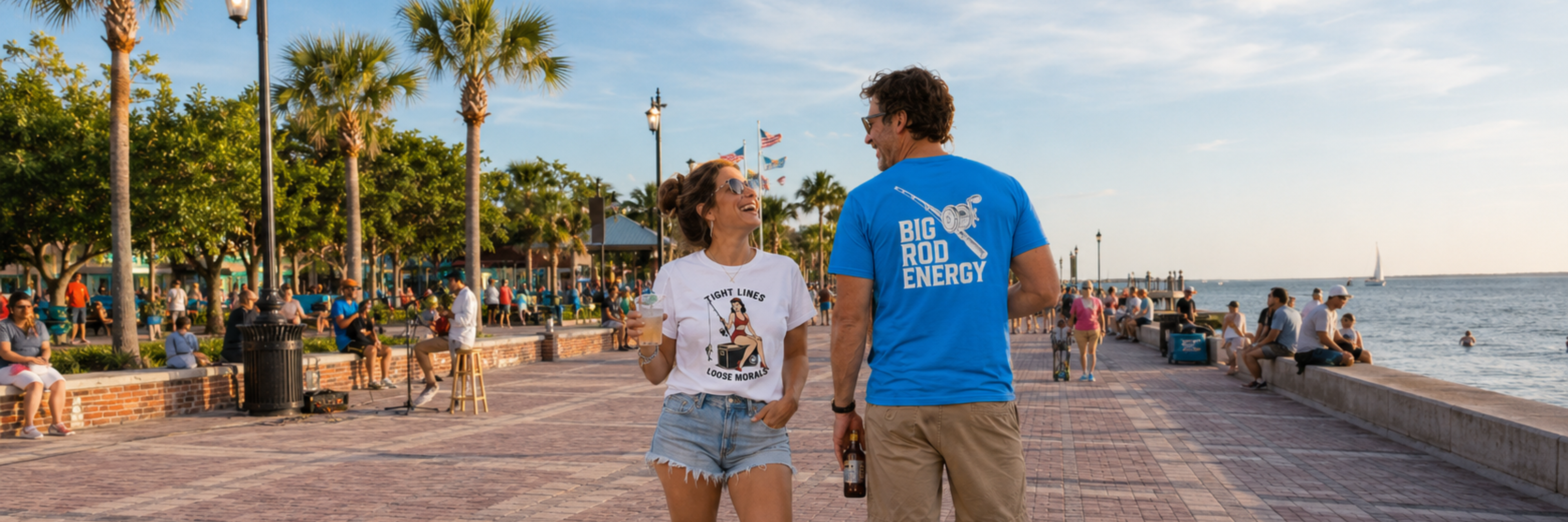 Salty Kiss men’s and women’s coastal graphic t-shirts worn on a sunny waterfront boardwalk.