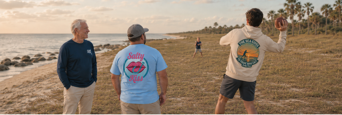 Salty Kiss men’s coastal lifestyle image featuring three men on a Florida beach at golden hour, wearing graphic tees and a hoodie, playing football by the ocean.