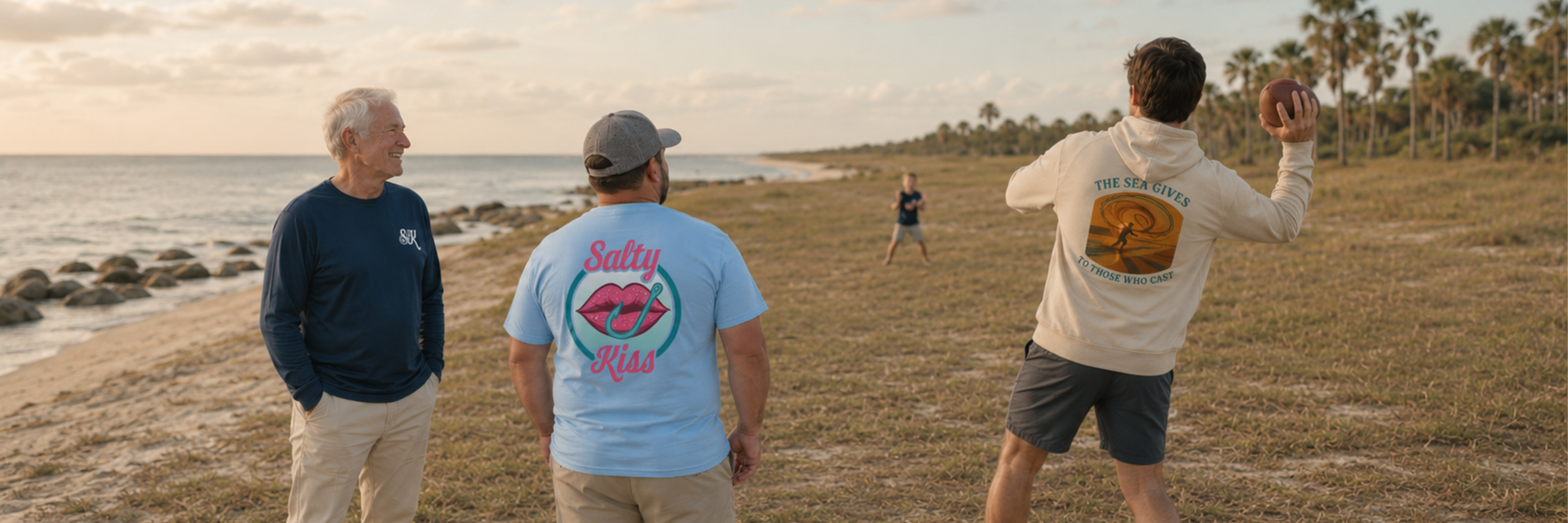 Salty Kiss men’s coastal graphic tees and hoodie worn during a beach football game by the ocean.