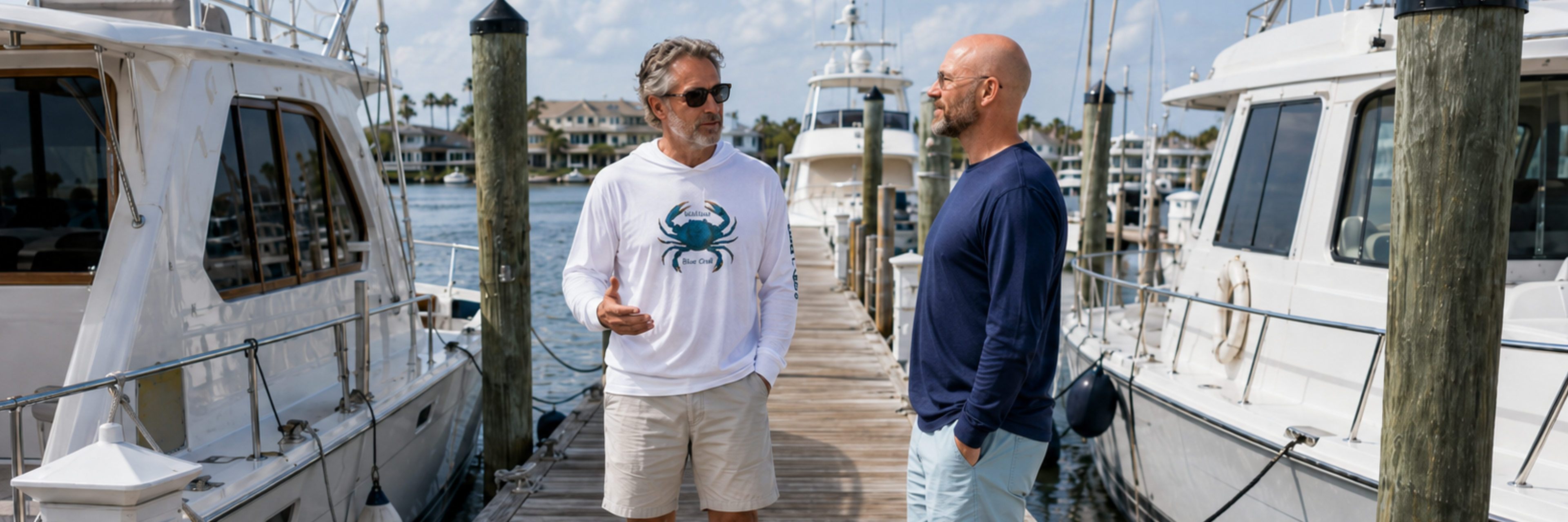 Salty Kiss men’s coastal long sleeve shirts worn on a marina dock with fishing boats in the background.